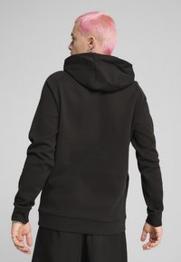 Sort hættetrøje med afslappet pasform, der har ribbetræk ved håndled og i kanten. Glat tekstur, ingen synlige mønstre og minimalistisk design.