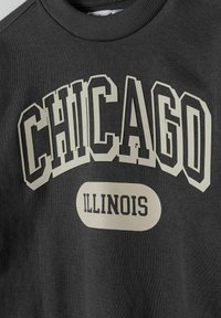 Sötét szürke pulóver, merész, rétegzett szöveggel: "CHICAGO" krémszínben és "ILLINOIS" feketében, ovális formában. Puha textúrájú.