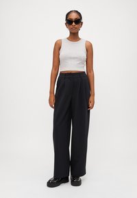Gray cropped tank top, black wide-leg trousers with pleats, and black platform shoes with studs; person wearing oversized black sunglasses.