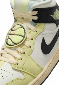 Chaussure de basketball montante en cuir crème et jaune pâle, avec un logo Nike swoosh noir, un logo Air Jordan et un patch de basketball sur les lacets.
