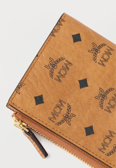 Καφέ δερμάτινο πορτοφόλι με λογότυπο MCM και σχέδιο διαμαντιών, με χρυσό φερμουάρ και σκούρο καφέ δερμάτινο προσχεδιασμό στο φερμουάρ. Υφή με ανάγλυφο φινίρισμα.