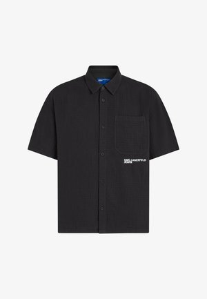 Czarna koszula na krótki rękaw z kołnierzykiem, kieszenią na piersi po lewej stronie oraz białym logo "KARL LAGERFELD JEANS" obok kieszeni.