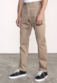 Beige bomuldsbukser med lige pasform, med knaplukning og sidelommer, parret med sorte sneakers og hvide snørebånd.