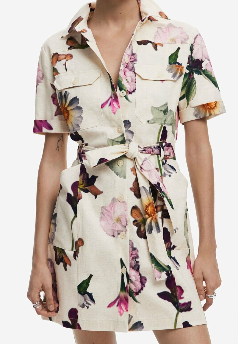 Robe crème à manches courtes avec fermeture à boutons sur le devant, imprimé floral, poches poitrine et ceinture en tissu nouée à la taille.