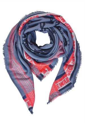 Lyseblåt og rødt firkantet tørklæde med zigzag-mønstre og delvist synlig fed tekst, foldet i en løs spiral med frynser på kanterne.