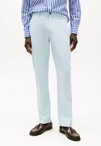 Pantalones de algodón azul claro con corte recto, combinados con una camisa de rayas azul y blanca. Mocasines marrones completan el conjunto.