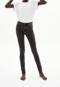 Jeans skinny de tiro alto en negro con una textura suave, diseño de cinco bolsillos y un ligero desgaste. Se llevan con una camiseta blanca holgada.
