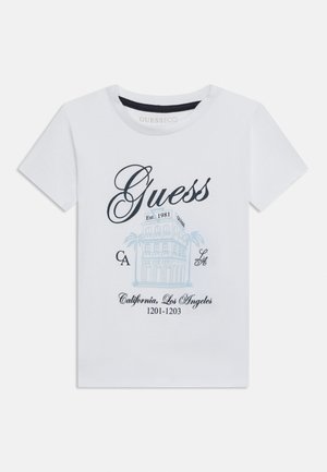 T-shirt bianca a maniche corte con logo "Guess", schizzo di un edificio con palme e testo "California, Los Angeles 1201-1203" in nero e blu.