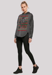 Tamno siva dukserica s kapuljačom s blagdanskom grafikom u crvenoj i zelenoj boji, uparena s crnim tajicama i crnim sportskim cipela.