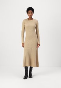 Abito a maglia con maniche lunghe in beige chiaro, con texture a coste, che arriva a metà polpaccio. Abbinato a stivali aderenti in pelle nera per creare un contrasto.