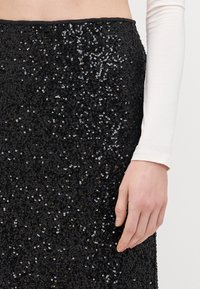 Zwarte paillettenrok met een aansluitend ontwerp, gekenmerkt door een gladde textuur en een glanzend oppervlak. Inclusief een subtiele, contrasterende tailleband.