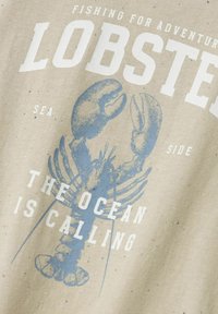 Beige bomulds-t-shirt med et blåt hummergrafik og teksten "HUMMERE," "HAVET KALDER," og en spraglet tekstur.