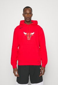 Červená mikina Nike s kapucňou s grafickým logom býka na prednej strane, obsahuje prednú vrecko, kapucňu so šnúrkou a rebrované manžety a lem.