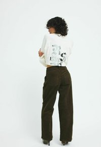 Vit oversized sweatshirt med abstrakta svarta mönster på ryggen, matchad med mörkbruna ribbade byxor med vida ben.