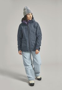 Waterproof blue jacket with a hood, purple inner lining, and front zip. Paired with light blue snow pants and beige boots.