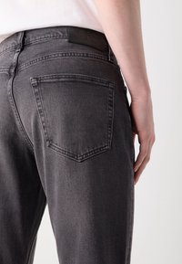 Grå denimjeans med en åtsittande design, som har en bakficka och en läderetikett i midjan. Slät textur och robust konstruktion.