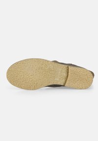 Sandal de color marrón con una suela de goma texturizada y un patrón elevado, complementada por un material superior suave y flexible. Diseño minimalista.