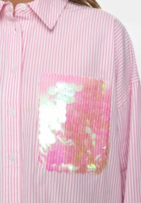 Roze en witte gestreepte shirt met een glanzende, pailletten zak met iriserende roze en zilveren kleuren. Met knopen, lichtgewicht stof.