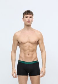 Sorte boxer briefs med en grøn talje, mærket "TOMMY HILFIGER." Stoffet ser glat og strækbart ud, tætsiddende til kroppen.