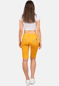 Geel denim bermudashorts met een slim fit ontwerp, voorzien van twee achterzakken en contrasterende stiksels. Gedragen met een witte crop top.