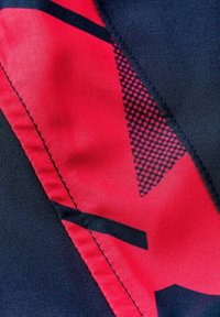Nahaufnahme eines Stoffs mit roten und schwarzen geometrischen Mustern und sichtbaren Nähten entlang der Naht.