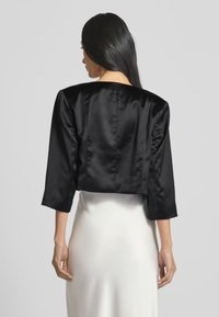 Giacca corta nera in satin con maniche a tre quarti e una superficie liscia, caratterizzata da un design semplice e senza hardware visibile.