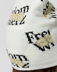Gorro de punto blanco con texto y gráficos en negro y beige. El diseño incluye "Libertad" y otras palabras en un patrón repetitivo.