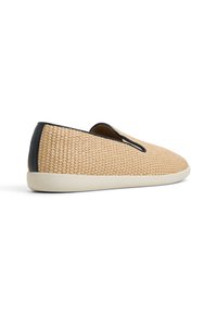 Flätad beiger textil slip-on sko med rund tå och svarta läderdetaljer, med en krämfärgad gummisula.