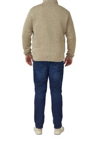 Pull beige en polaire avec col montant, vue de dos. Associé à un jean en denim bleu et des chaussures claires. Détail du tissu texturé visible.