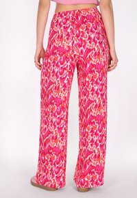 Roze luipaardprint broek met een losse, wijde pasvorm, voorzien van een elastische tailleband en zachte stof, gezien vanuit de achterkant.