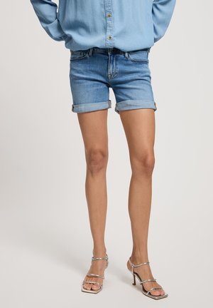 Jasnoniebieskie dżinsowe szorty z podwiniętymi mankietami, o średnim zabarwieniu, w fasonie slim fit. Połączone z srebrnymi sandałami na wysokim obcasie z paskami.