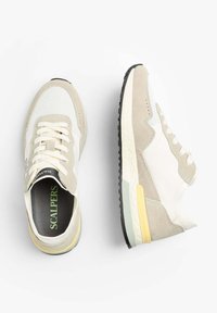 Sneakers z połączeniem beżowego zamszu i białej siateczki, z czarną gumową podeszwą. Zielone logo "SCALPERS" na wkładce i żółty akcent na pięcie.