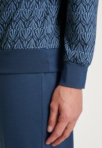 Marineblauwe langemouwtop met een geometrisch patroon in lichtblauw. Ribgebreide manchetten en zoom. Gladde textuur met een aansluitend ontwerp.