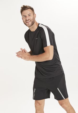 Sort atletisk T-shirt med hvide ærmer, parret med sorte shorts med reflekterende detaljer. Fremstillet af letvægts og åndbart materiale.