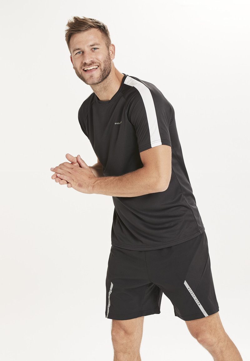 Musta urheilupaita valkoisilla hihoilla, yhdistettynä mustiin shortseihin, joissa on heijastavia yksityiskohtia. Valmistettu kevyestä ja hengittävästä materiaalista.