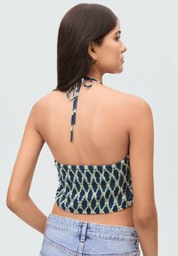 Námornícky modrý crop top s textúrovaným vzorom v svetlejších odtieňoch, s halter krkom a viazaním, elastický pás na spodnej strane, nosený s svetlými džínsovými šortkami.