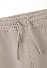 Beige sweatpants hebben een elastische tailleband met een trekkoord, zachte katoenen stof en gedetailleerde stiksels langs de naden.