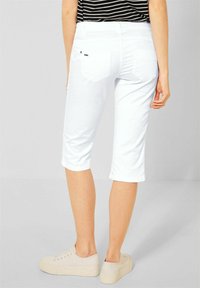 Bílé bavlněné capri kalhoty s vypasovaným střihem, s ohrnutými manžetami a dvěma zadními kapsami. V kombinaci se světlými teniskami.