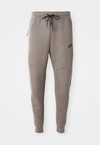Szare dresy Nike z elastycznym pasem ze sznurkowym zapięciem, zwężanymi nogawkami, bocznymi kieszeniami i wyraźnymi detalami szwów. Miękka, teksturowana tkanina.