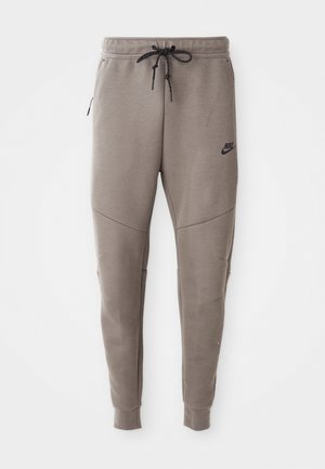 Gray Nike sweatpants with a drawstring waistband, tapered legs, side pockets, and distinct seam detailing. Soft, textured fabric.