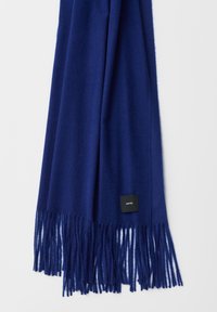 Sciarpa blu navy in tessuto morbido con dettagli di frange alle estremità. Presenta un piccolo tag nero con testo bianco.