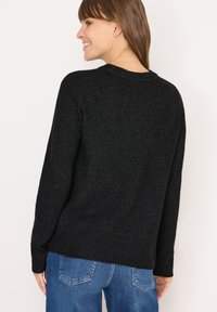 Maglione nero lavorato a maglia con maniche lunghe e scollatura rotonda. Presenta una texture sottile e una vestibilità comoda. Abbinato a jeans blu.