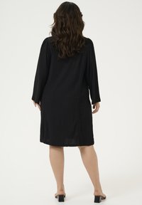Vestido negro con mangas largas y tela texturizada, con detalles en las costuras laterales. Combinado con sandalias de tacón con espalda descubierta.
