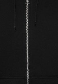 Felpa nera con zip realizzata in tessuto morbido, dotata di zip metallica e coulisse, con una texture liscia e senza motivi visibili.