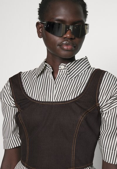 Robe en denim marron avec un col rond, chemise rayée blanche et noire en dessous, et détails de couture orange contrastants.