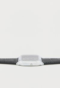 Stříbrné obdélníkové hodinky s černým koženým řemínkem, skleněným ciferníkem, stříbrnými doplňky a jednoduchým černým ciferníkem s ukazateli.