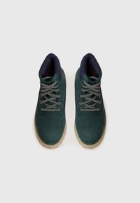 Stivali ankle in suede verde scuro con lacci grigi, colletto imbottito blu navy e suola in gomma beige, caratterizzati da una texture liscia e design con punta arrotondata.