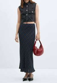 Zugeschnittene schwarze Jeansweste mit Taschen, karierte Maxirock in Blau und Schwarz, glänzende schwarze spitze High Heels und eine rote Handtasche mit Nieten.