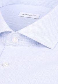 Chemise texturée bleu clair avec des boutons blancs et une étiquette de marque « seidensticker » visible à l'intérieur du col.