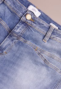 Světlé modré džíny z denimu s mosazným knoflíkem, žlutým prošitím, dvěma předními kapsami a značkovou nášivkou na pásku. Vyrobeno v Itálii.